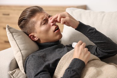 Young man with tissue suffering from sinusitis and lying in bed at home