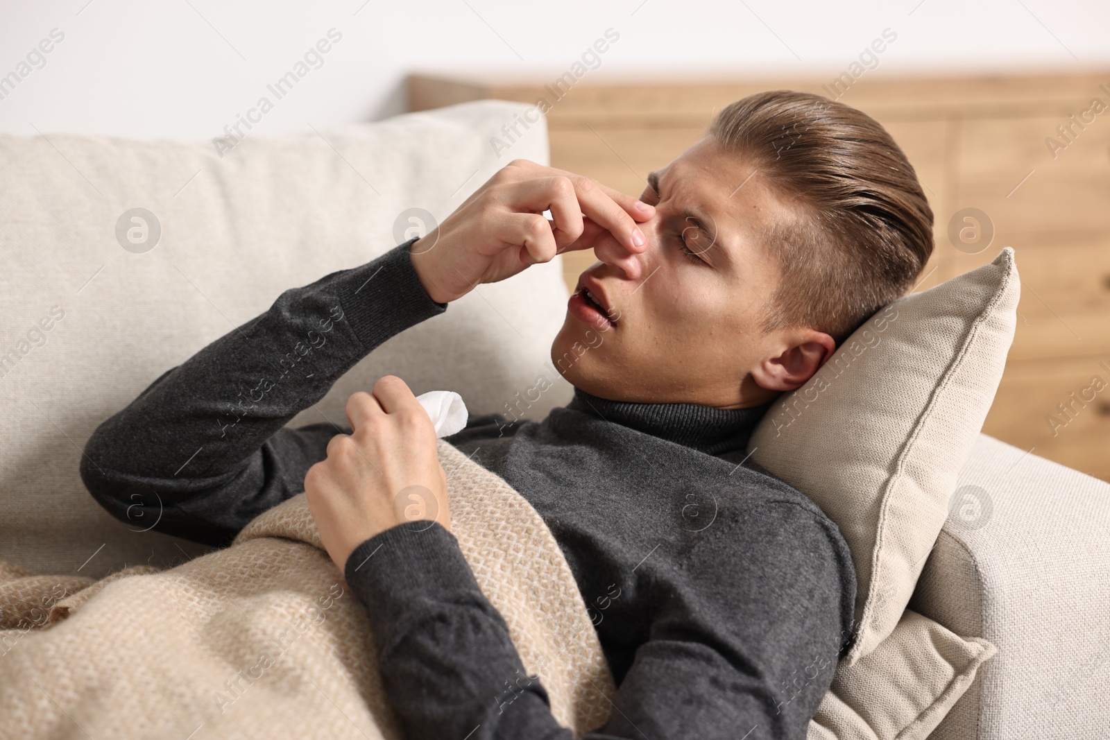 Photo of Young man with tissue suffering from sinusitis and lying in bed at home