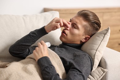 Young man with tissue suffering from sinusitis and lying in bed at home