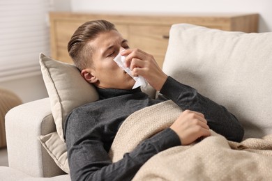 Young man with tissue suffering from sinusitis and lying in bed at home