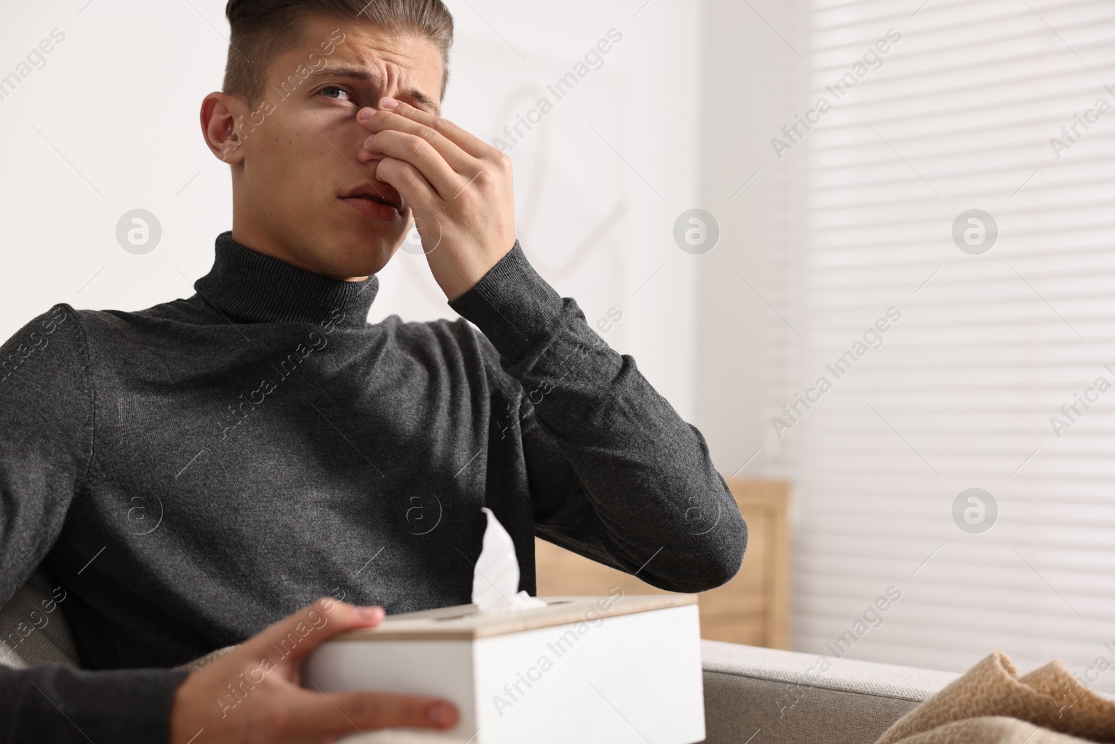 Photo of Young man with tissues suffering from sinusitis at home, space for text