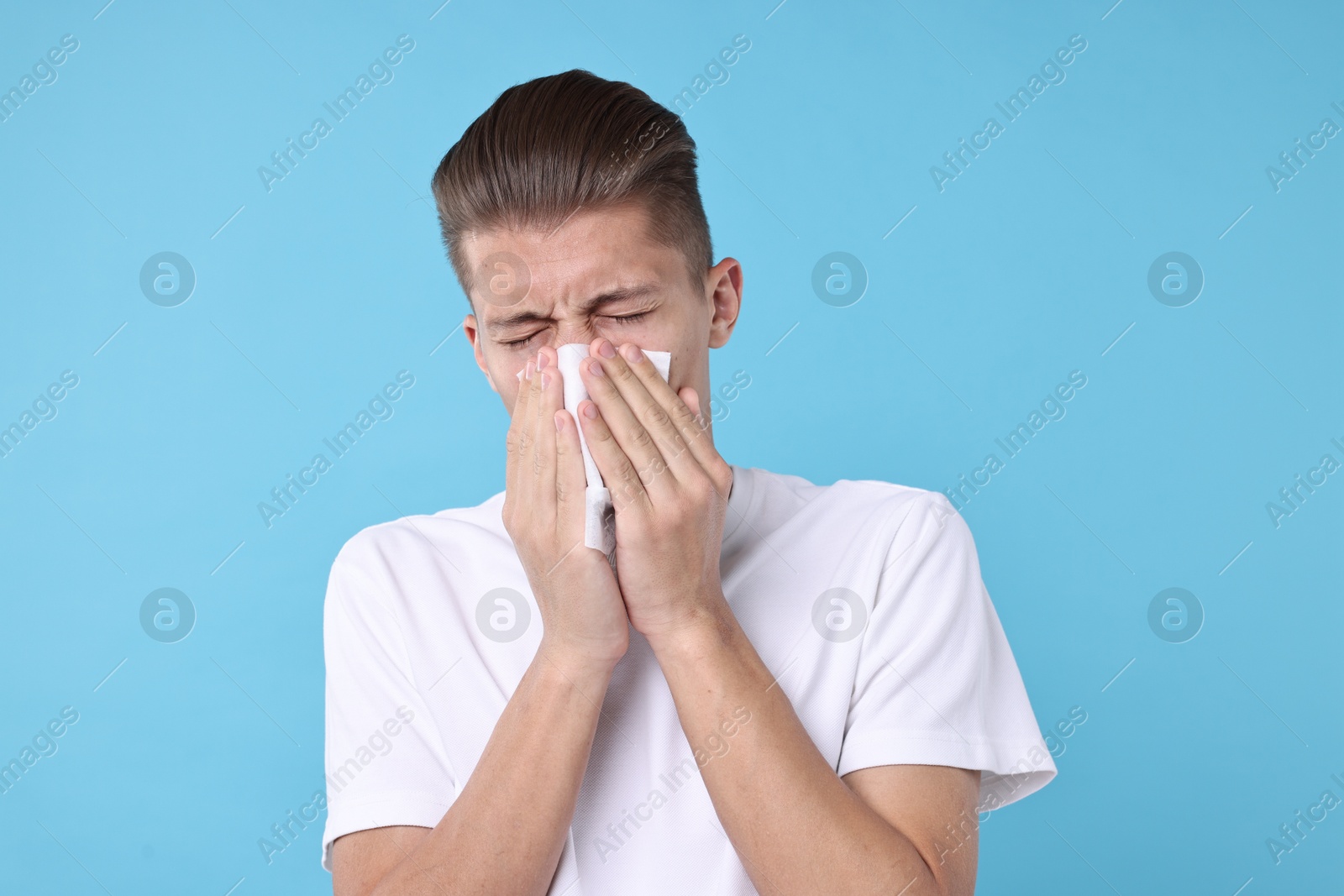 Photo of Young man with tissue suffering from sinusitis on light blue background