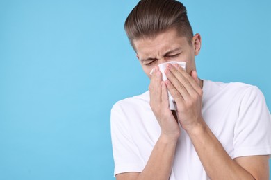 Photo of Young man with tissue suffering from sinusitis on light blue background, space for text