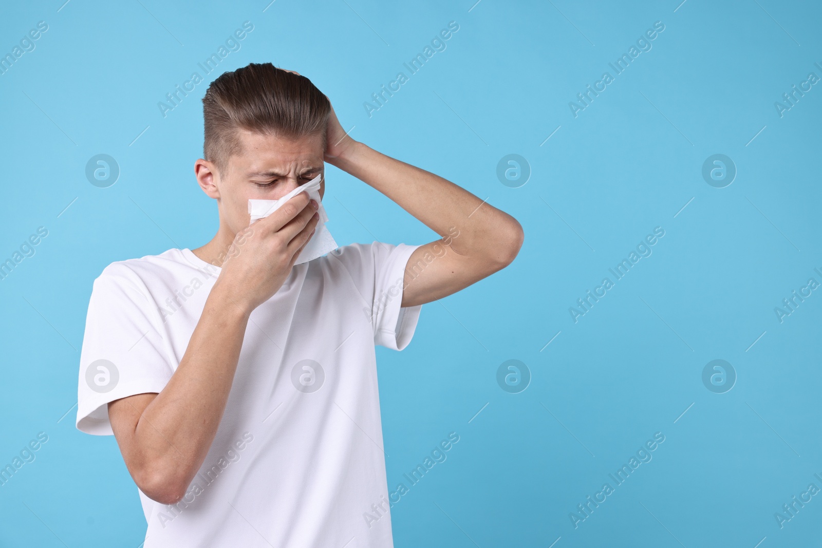 Photo of Young man with tissue suffering from sinusitis on light blue background, space for text