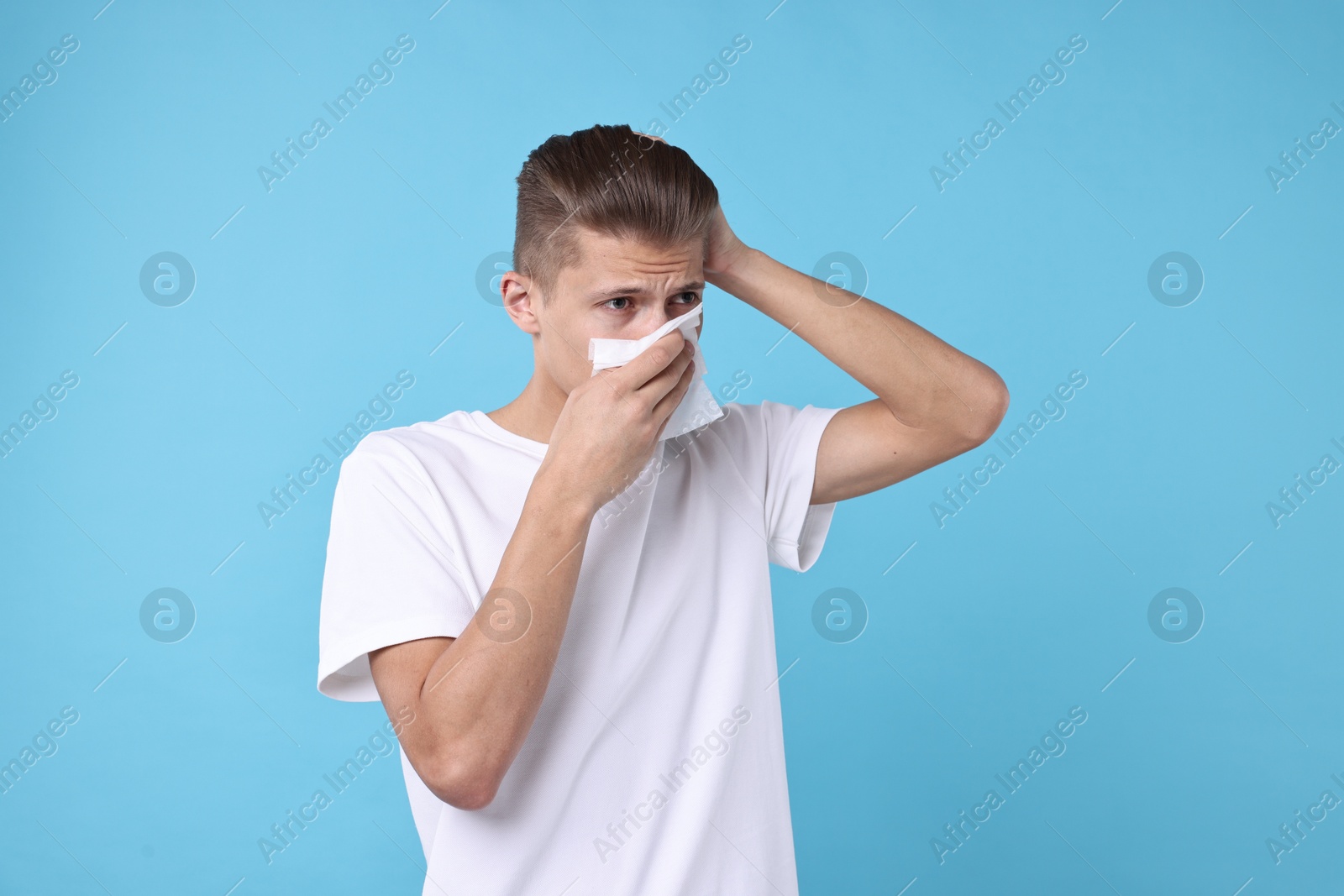 Photo of Young man with tissue suffering from sinusitis on light blue background