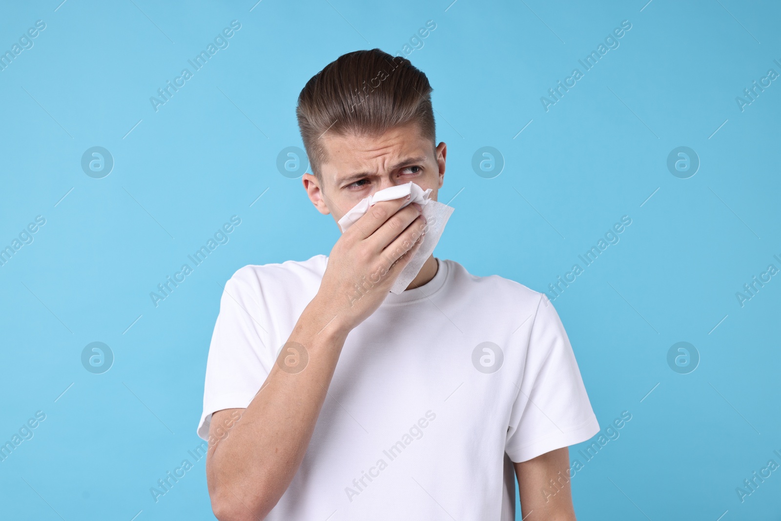 Photo of Young man with tissue suffering from sinusitis on light blue background