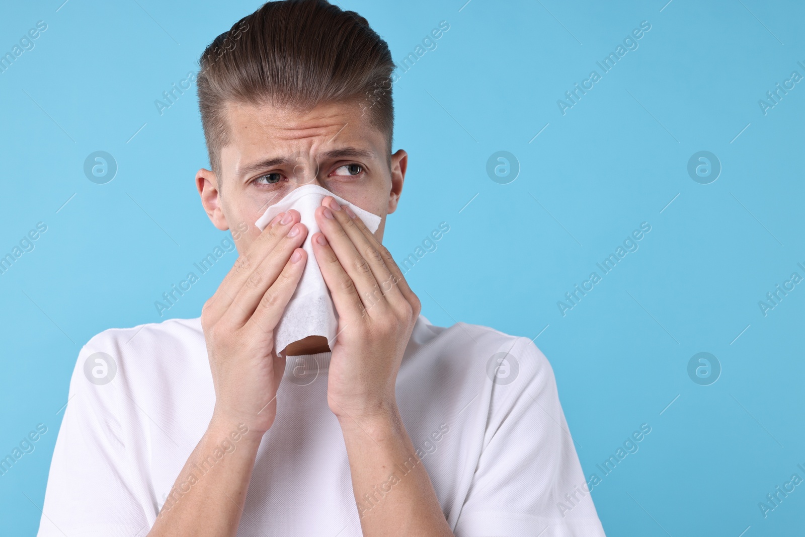 Photo of Young man with tissue suffering from sinusitis on light blue background, space for text