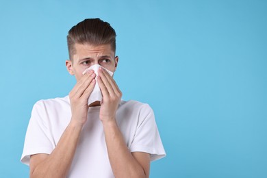 Young man with tissue suffering from sinusitis on light blue background, space for text