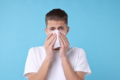 Photo of Young man with tissue suffering from sinusitis on light blue background