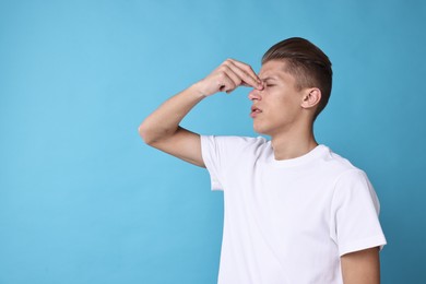 Photo of Young man suffering from sinusitis on light blue background, space for text