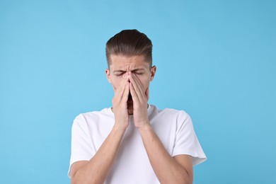 Photo of Young man suffering from sinusitis on light blue background