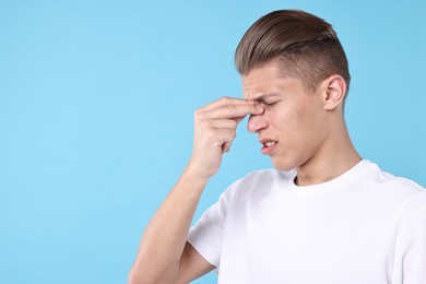 Young man suffering from sinusitis on light blue background, space for text