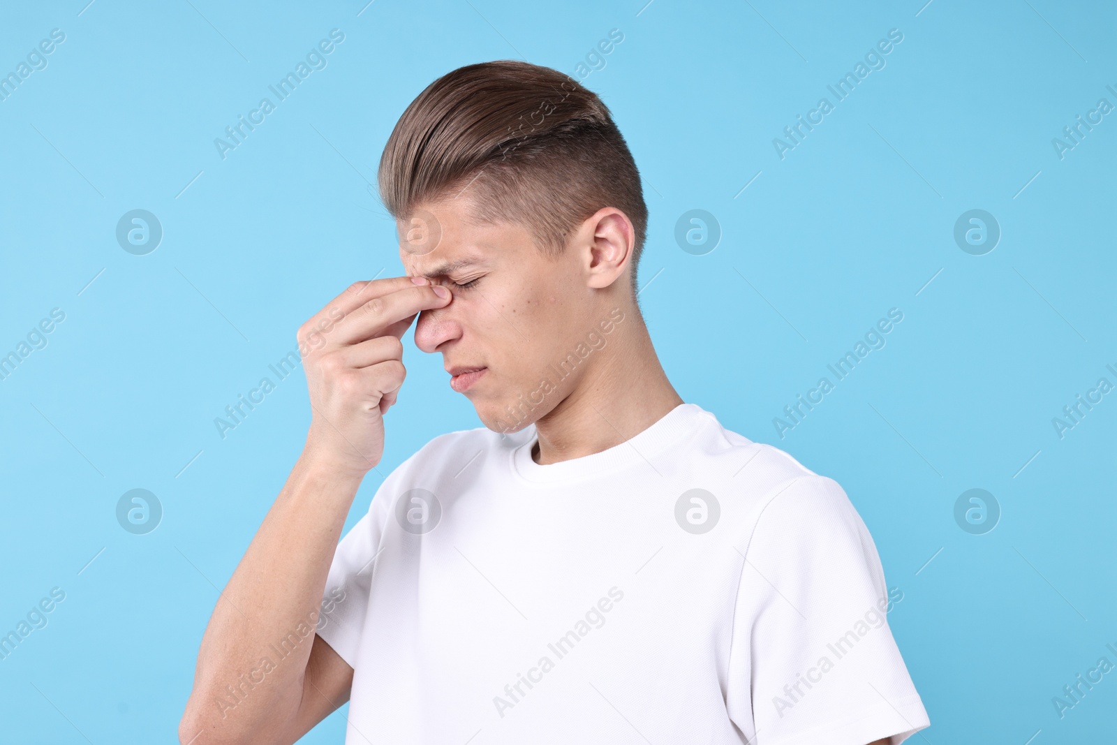 Photo of Young man suffering from sinusitis on light blue background