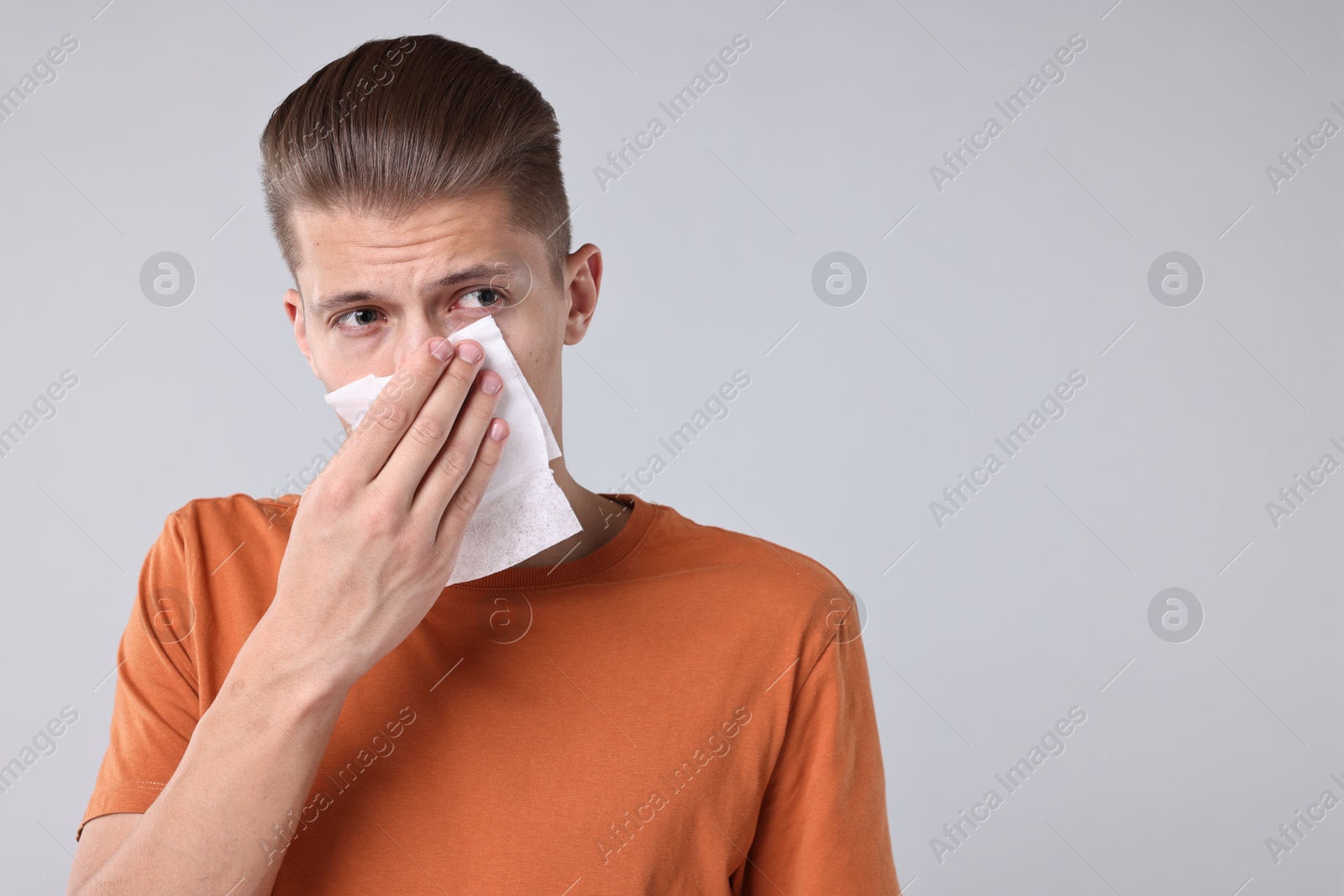 Photo of Young man with tissue suffering from sinusitis on light grey background, space for text