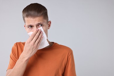 Young man with tissue suffering from sinusitis on light grey background, space for text