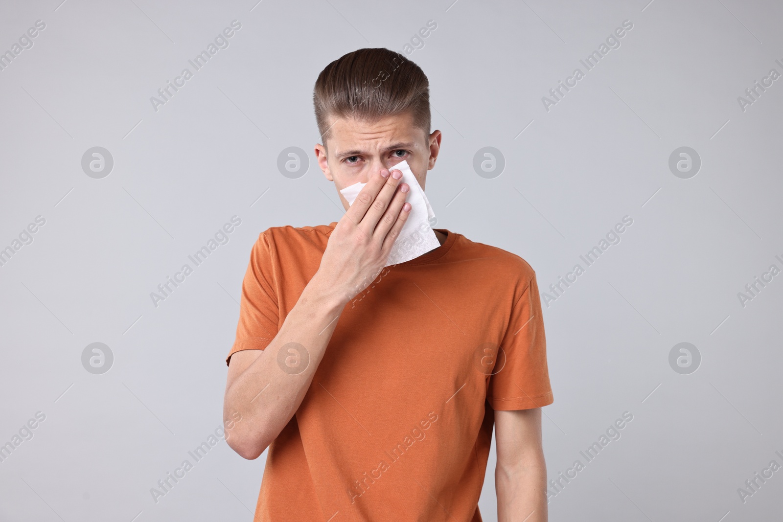 Photo of Young man with tissue suffering from sinusitis on light grey background