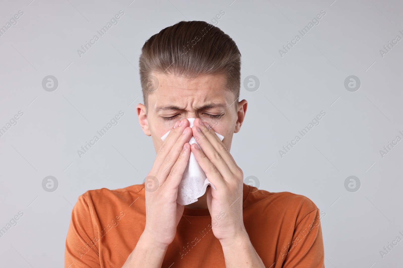 Photo of Young man with tissue suffering from sinusitis on light grey background