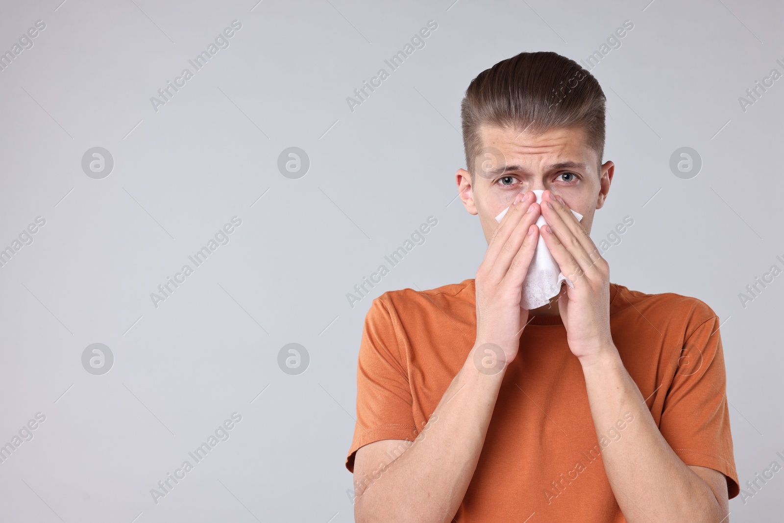 Photo of Young man with tissue suffering from sinusitis on light grey background, space for text