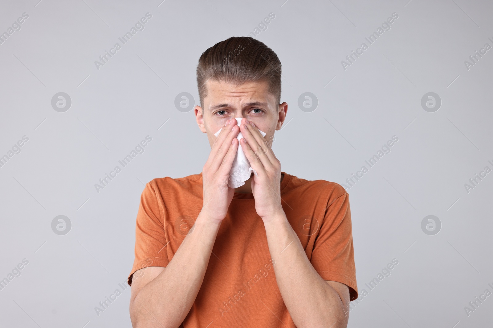 Photo of Young man with tissue suffering from sinusitis on light grey background