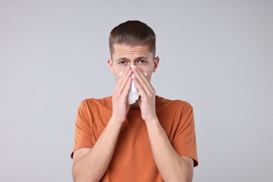 Photo of Young man with tissue suffering from sinusitis on light grey background