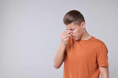 Young man suffering from sinusitis on light grey background, space for text