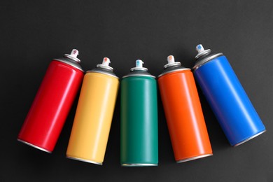 Photo of Many spray paint cans on dark gray background, top view