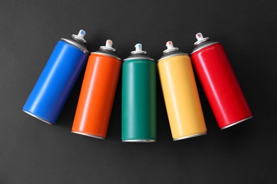 Photo of Many spray paint cans on dark gray background, top view