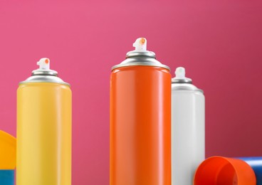 Many spray paint cans on pink background, closeup