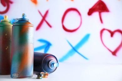 Many spray paint cans near white wall with different drawn symbols, space for text