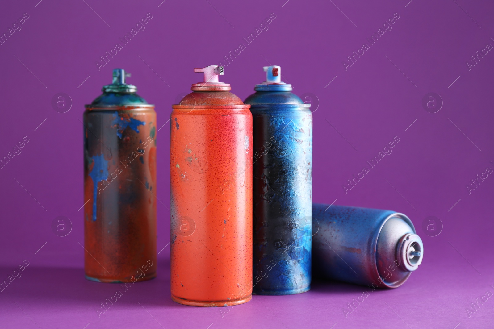 Photo of Many spray paint cans on violet background