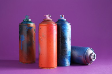 Many spray paint cans on violet background