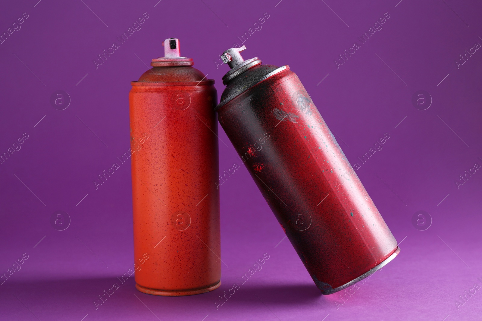 Photo of Two spray paint cans on violet background