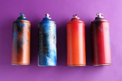 Many spray paint cans on violet background, top view