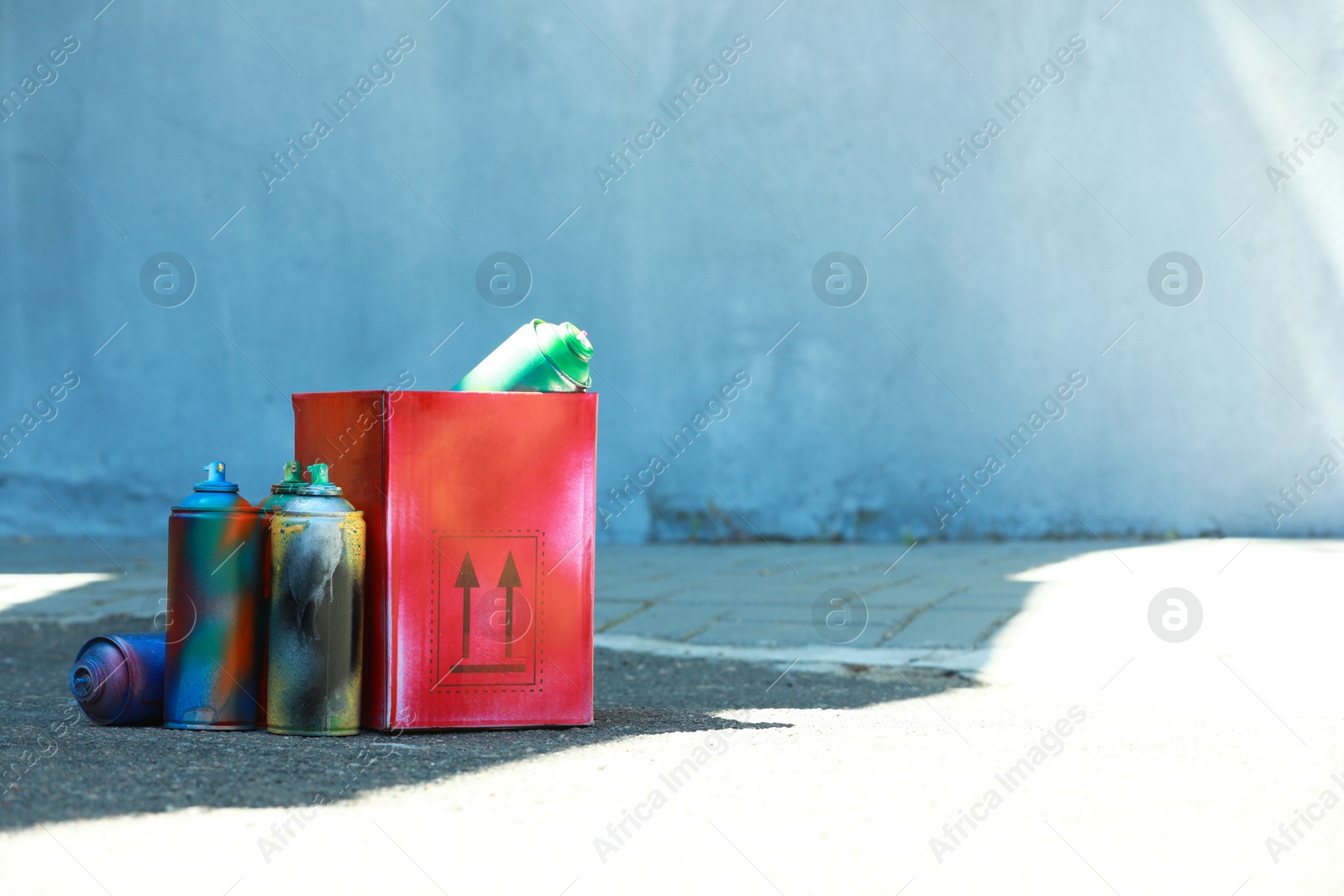 Photo of Many spray paint cans and red cardboard box outdoors, space for text