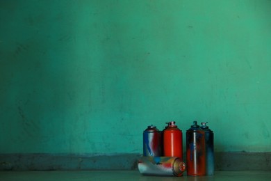 Many spray paint cans near green wall, space for text