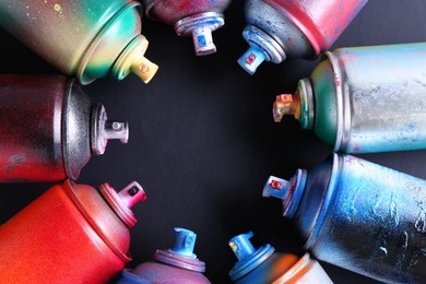 Many spray paint cans on black background, flat lay