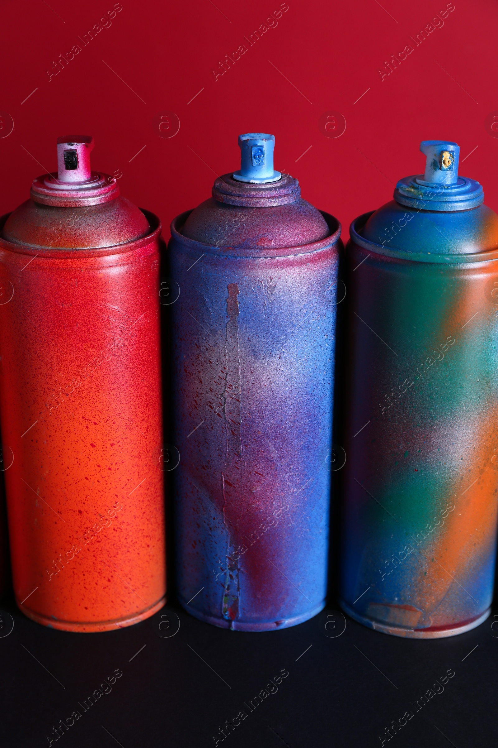 Photo of Many spray paint cans on black surface against red background, closeup