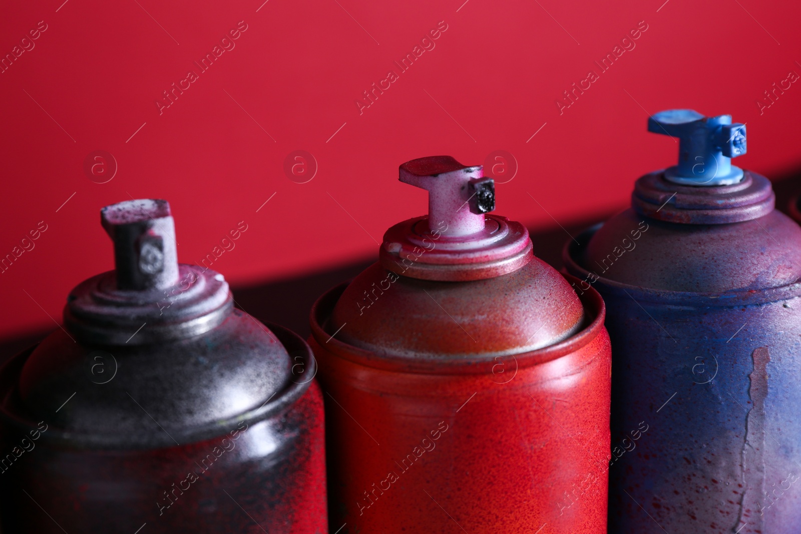 Photo of Many spray paint cans on red background, closeup