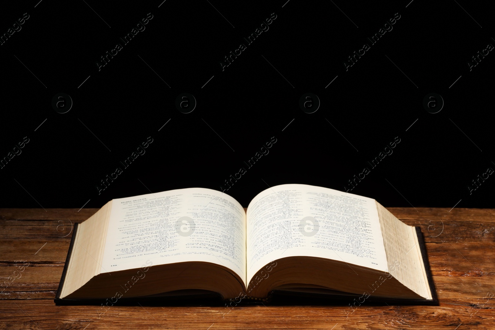 Photo of Bible on wooden table against black background, space for text. Religion of Christianity