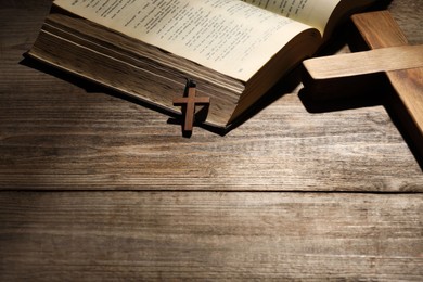 Photo of Bible and crosses on wooden table, space for text. Religion of Christianity