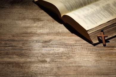 Photo of Bible and cross on wooden table, space for text. Religion of Christianity