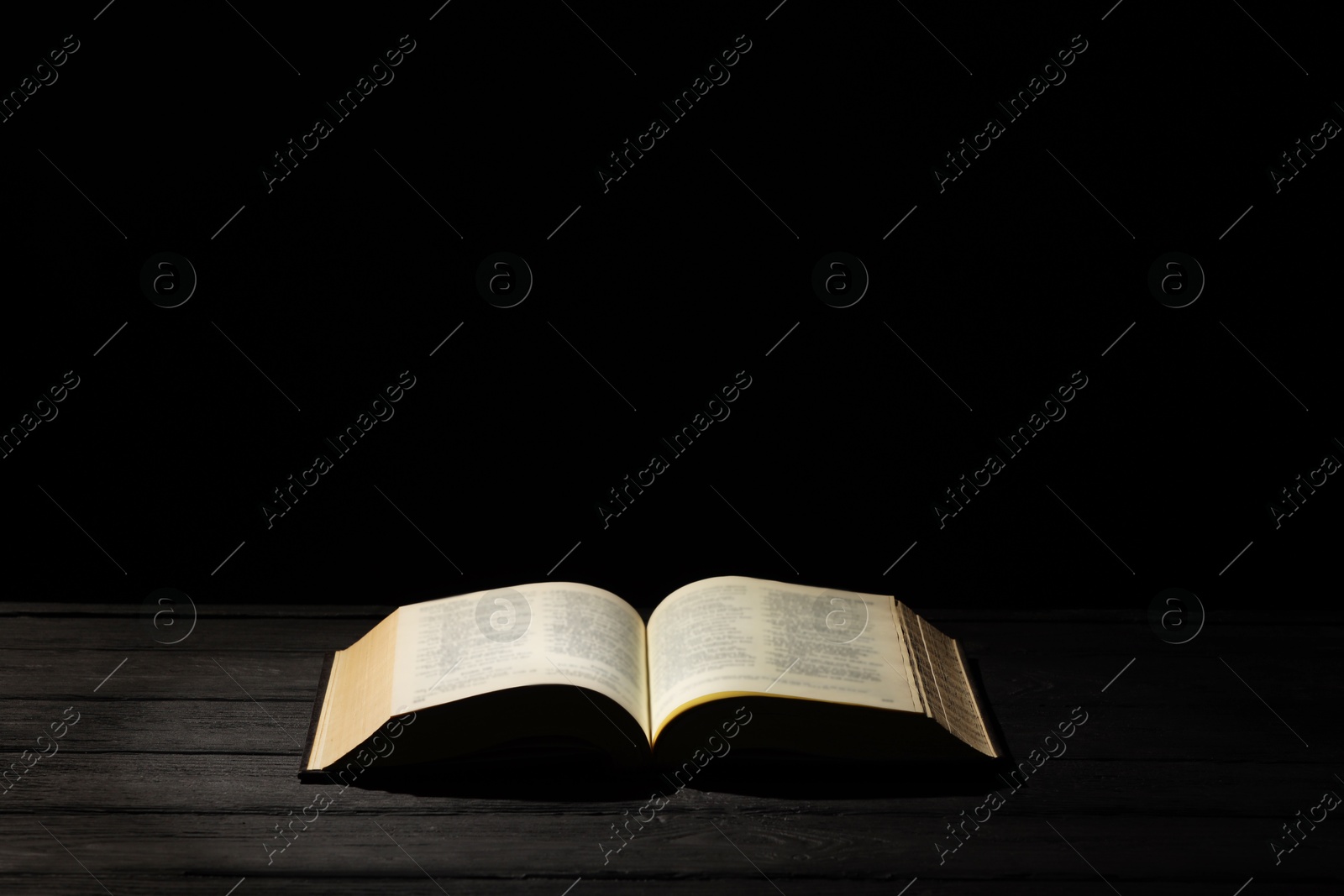 Photo of Bible on dark wooden table against black background, space for text. Religion of Christianity