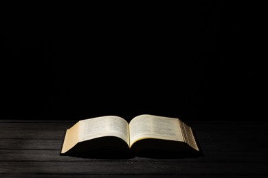 Bible on dark wooden table against black background, space for text. Religion of Christianity