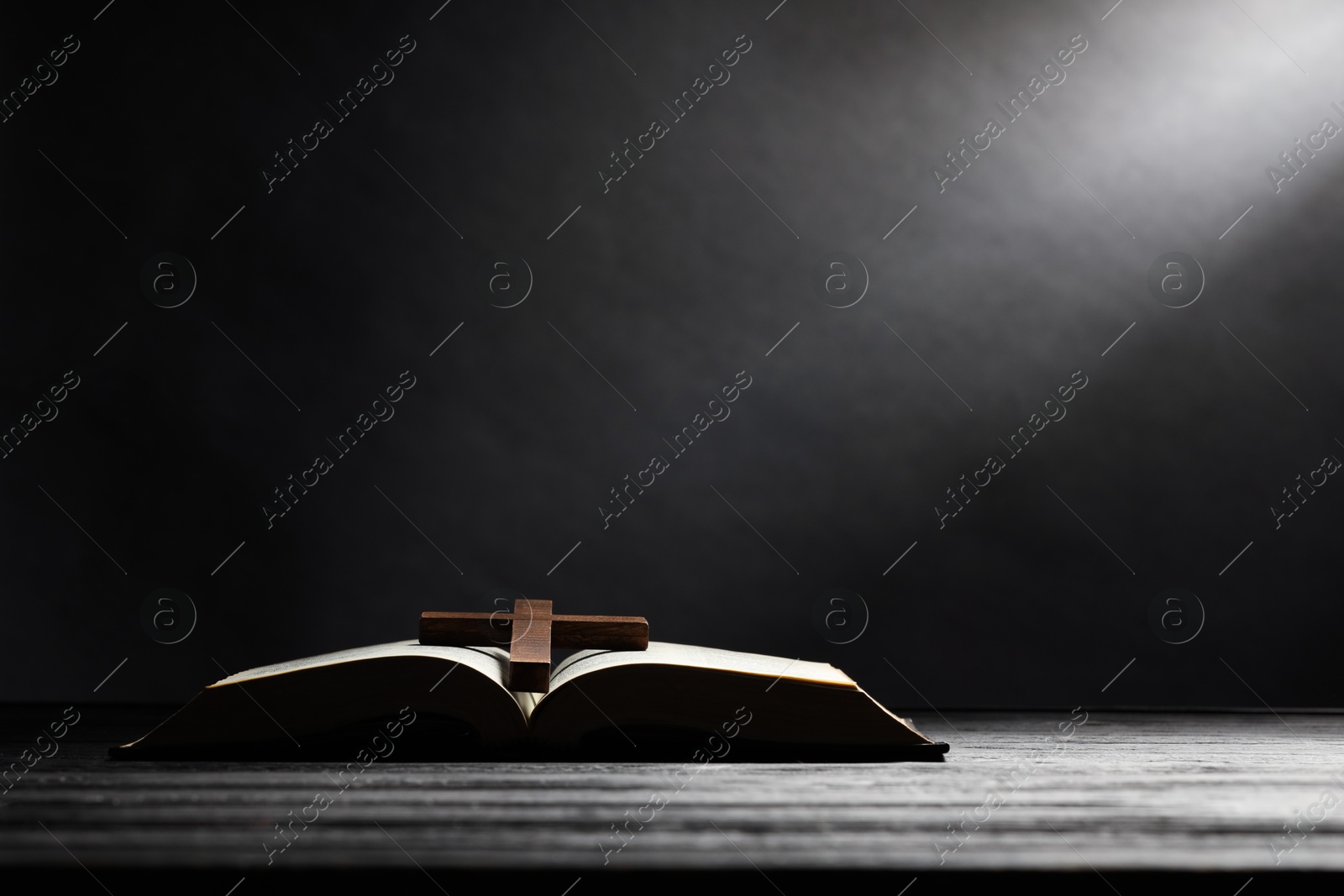 Photo of Bible and cross on gray wooden table against dark background, space for text. Religion of Christianity