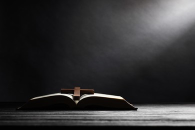 Photo of Bible and cross on gray wooden table against dark background, space for text. Religion of Christianity