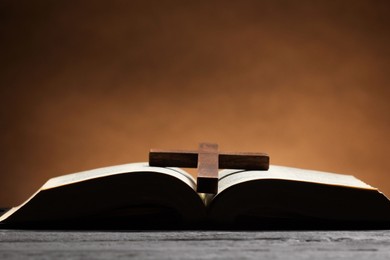 Photo of Bible and cross on gray table against brown background, space for text. Religion of Christianity