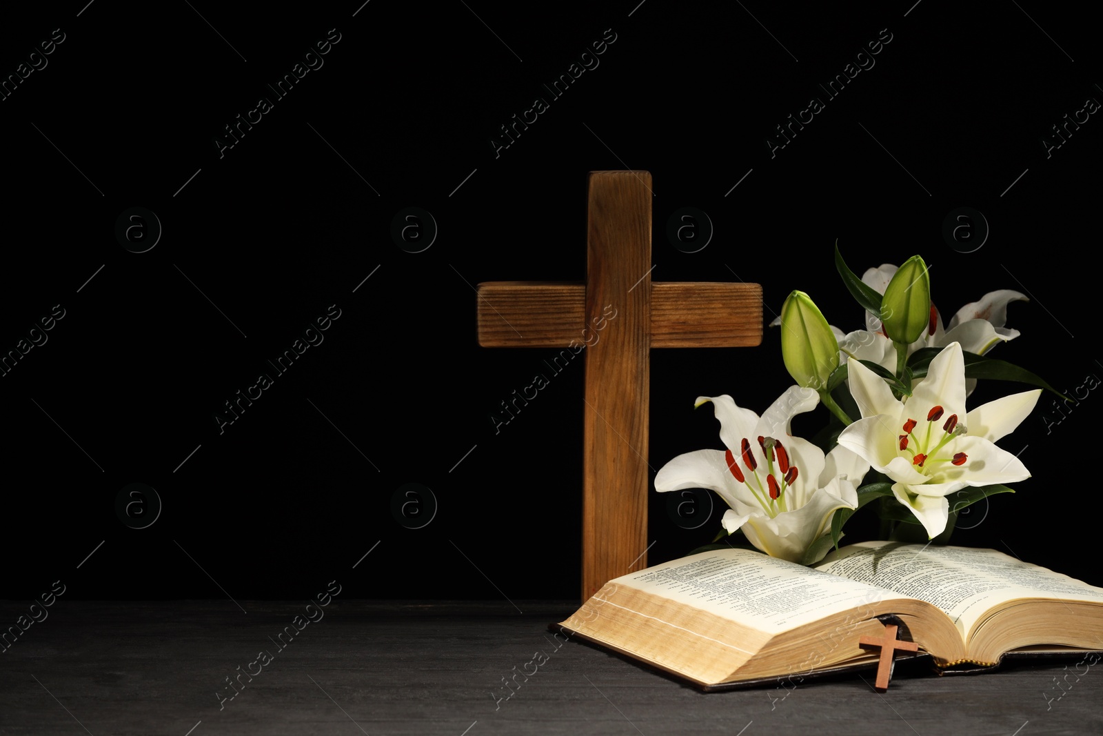 Photo of Bible, crosses and lilies on dark gray wooden table against black background, space for text. Religion of Christianity