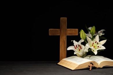 Photo of Bible, crosses and lilies on dark gray wooden table against black background, space for text. Religion of Christianity