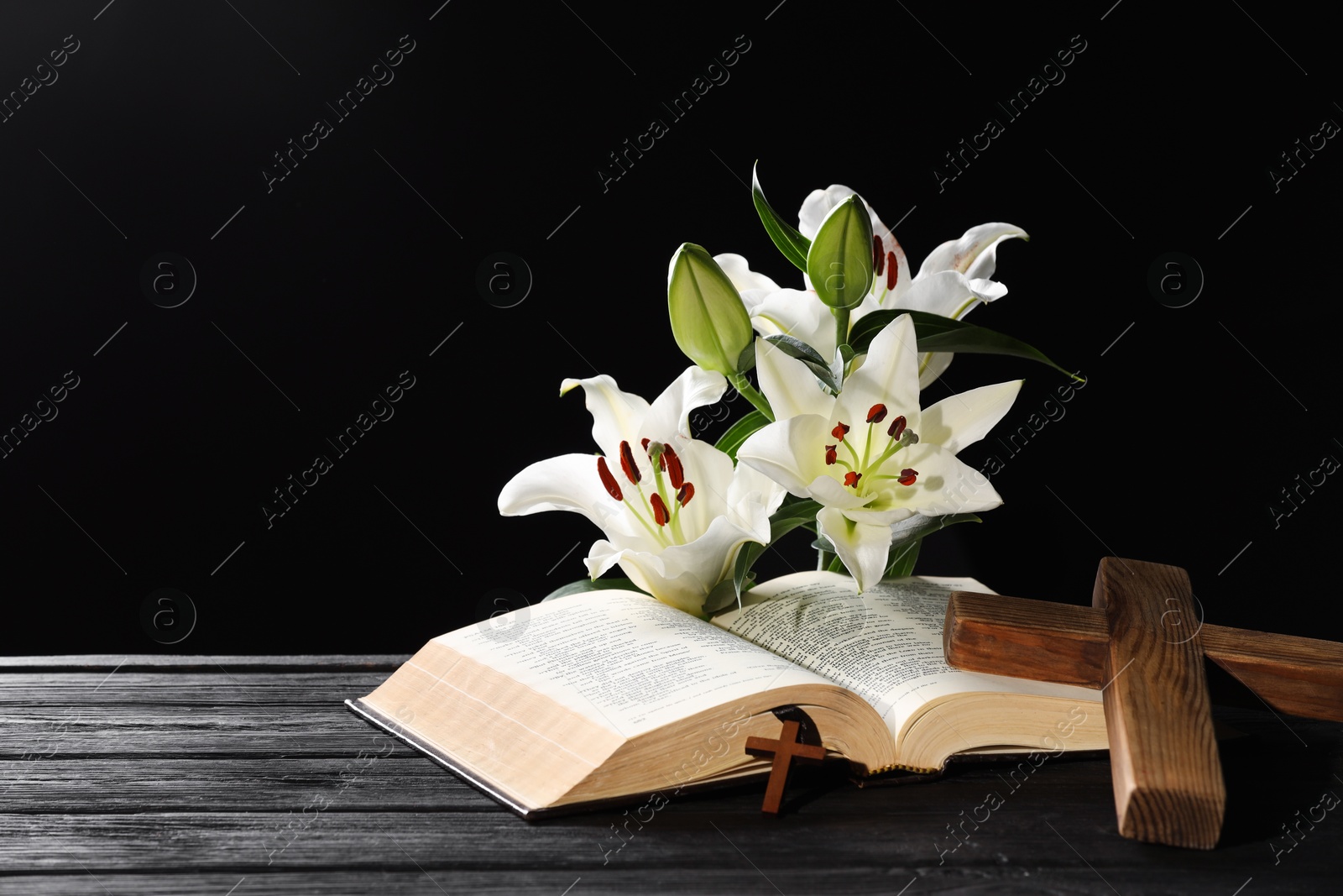 Photo of Bible, crosses and lilies on dark gray wooden table against black background, space for text. Religion of Christianity