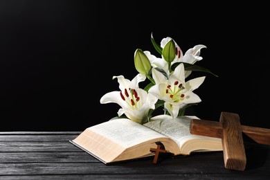 Photo of Bible, crosses and lilies on dark gray wooden table against black background, space for text. Religion of Christianity